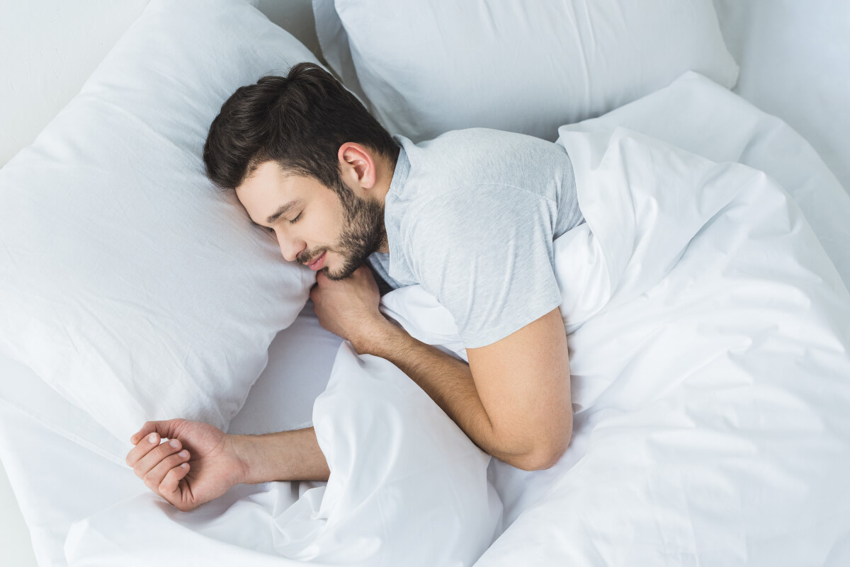 Man asleep in a bed with cozy, white bedding 