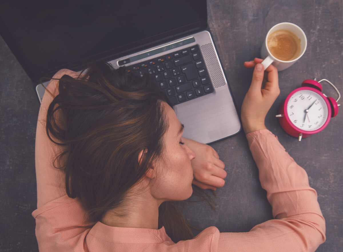 Woman asleep on her laptop holding a cup of coffee 