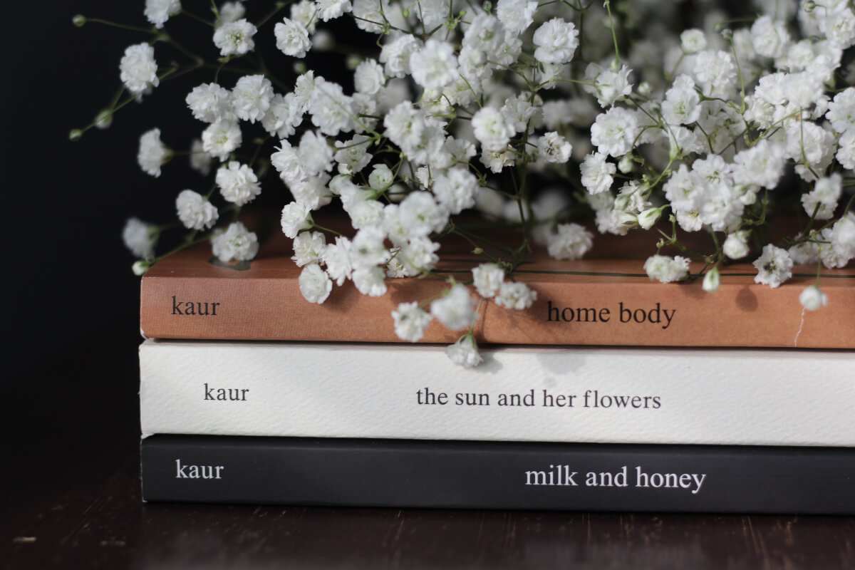Stack of books by Instapoet Rupi Kaur topped with a bundle of white flowers
