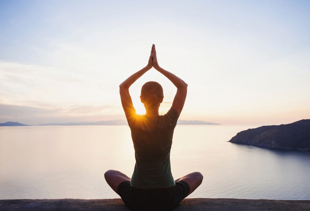 a woman meditating near the ocean at sunset