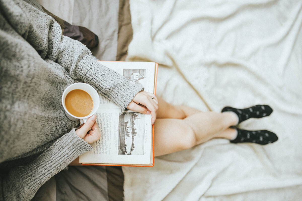 Person sitting in a cozy spot with a book and a cup of coffee. 