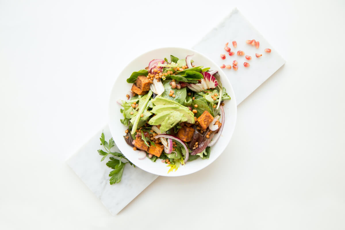 A delicious green salad is pictured, featuring avocado, tofu, red onion, and pine nuts. 