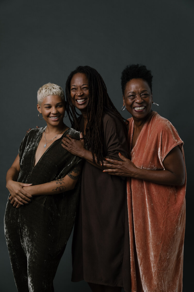 Women are happy to be wearing sustainable clothing from Miranda Bennett Studio. They are wearing long dresses colored with natural dyes in green and brown shades. 