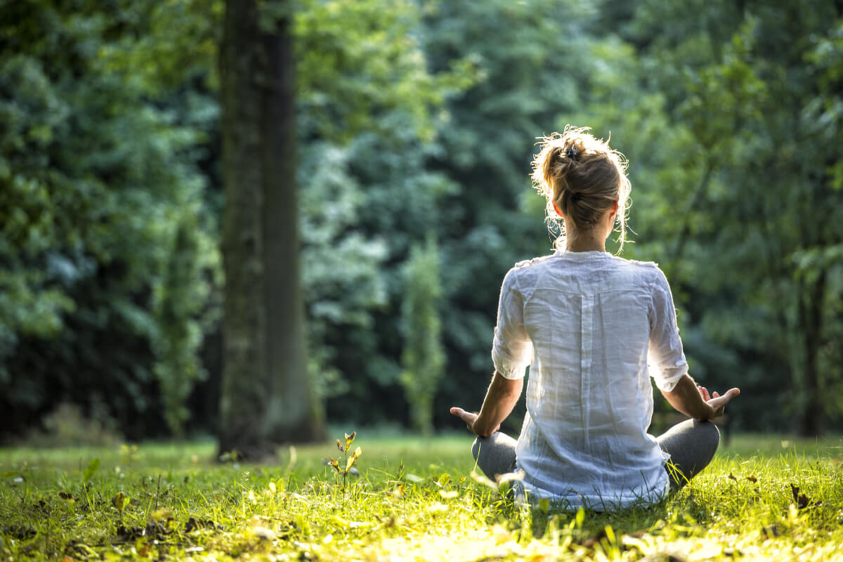 Woman sits cross-legged in the grass thinking about the best wellness apps.