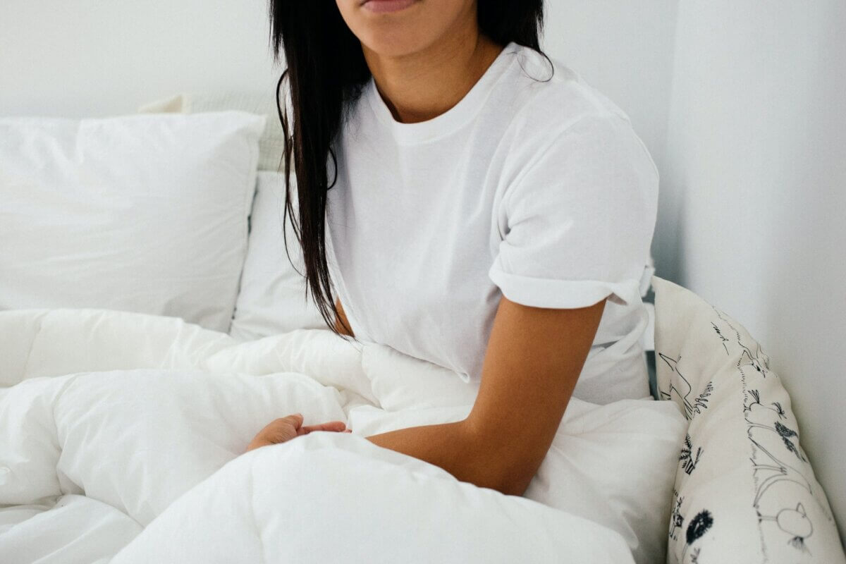 Woman sitting in cozy, white bedding. 