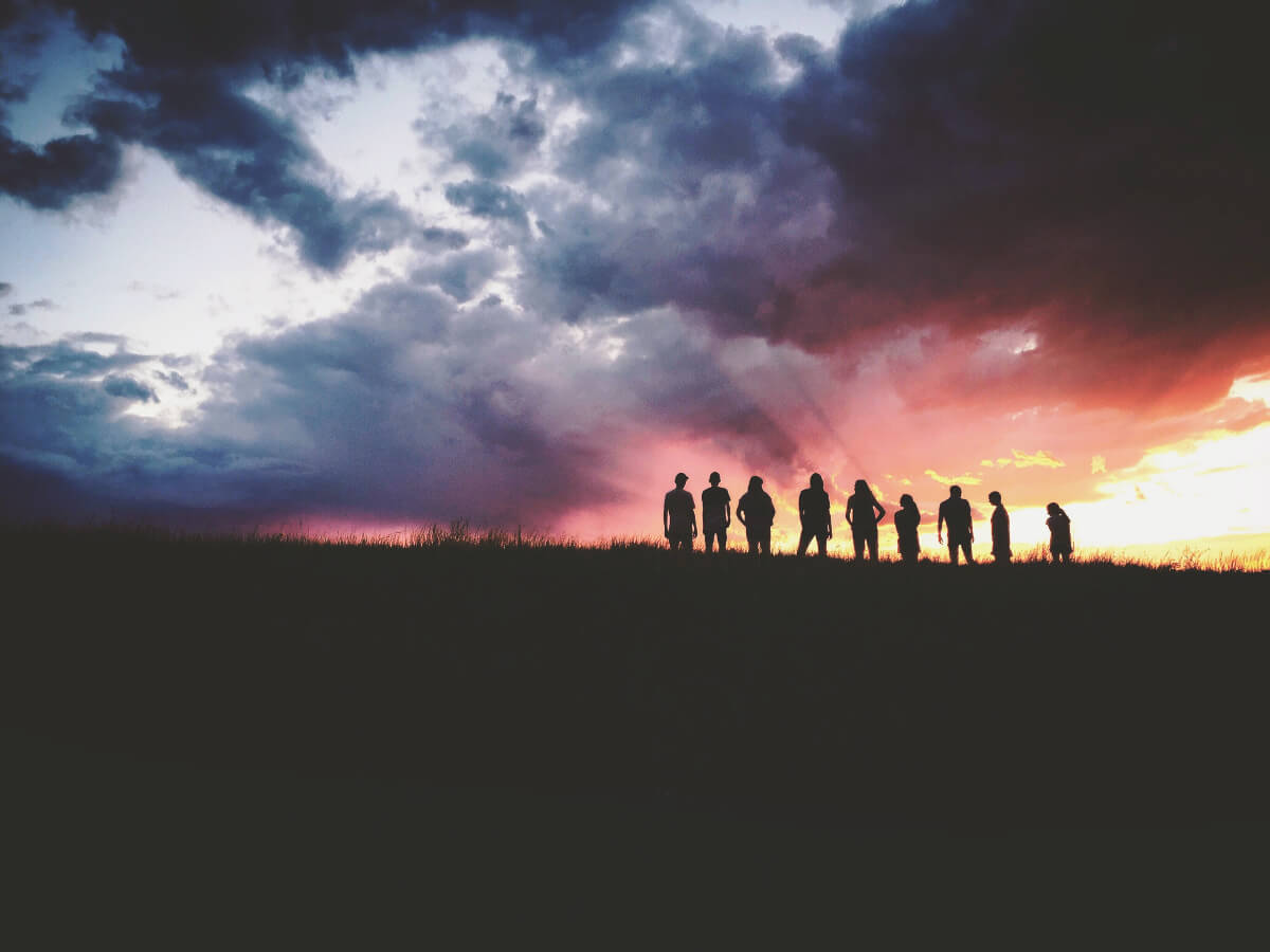 silhouettes of people with sunset and clouds in the background
