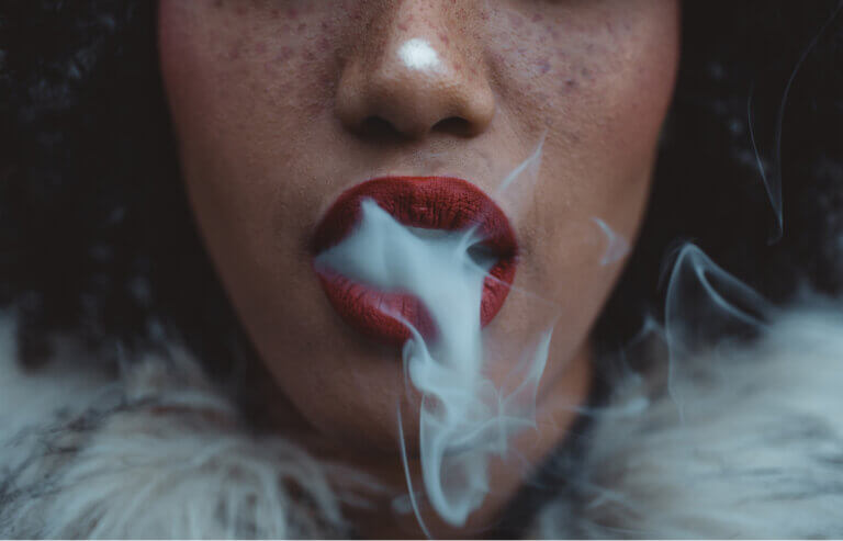 Woman wearing red lipstick exhaling cannabis smoke