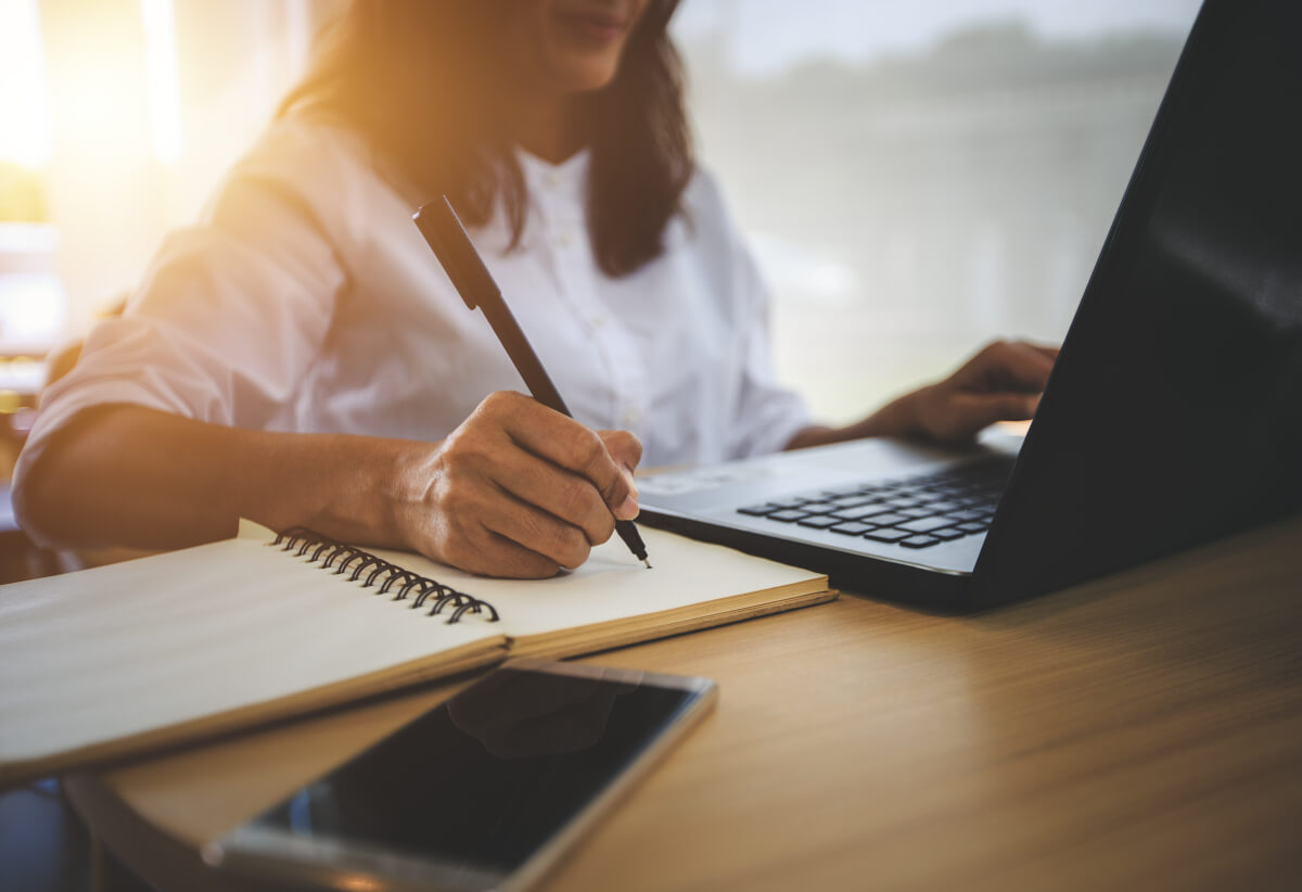 Person working on their laptop and making notes in a notebook