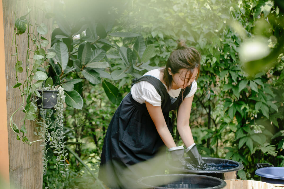 Woman making DIY natural plant dyes outdoors surrounded by greenery