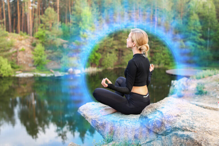 Woman sitting in the lotus position in nature surrounded by a blue ring of light