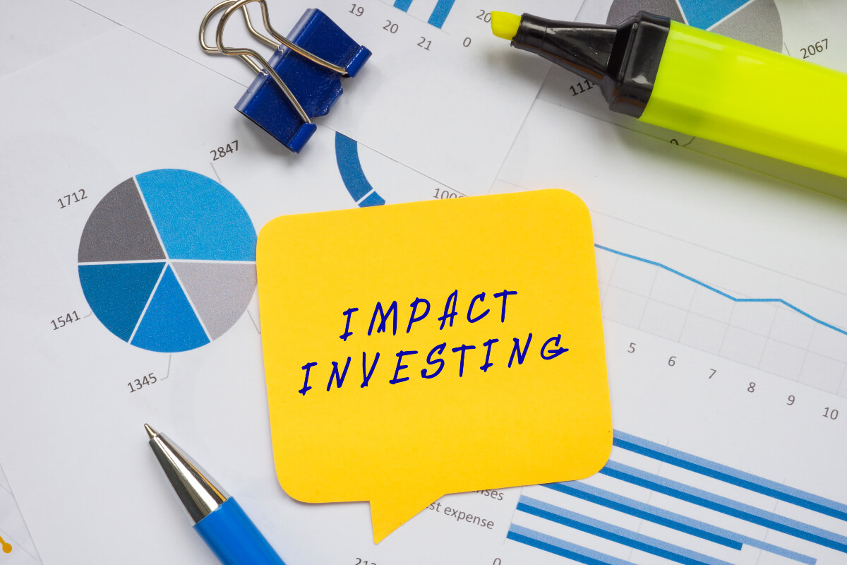 "Impact investing" is written on a yellow sticky note on top of a pile of charts and graphs. 
