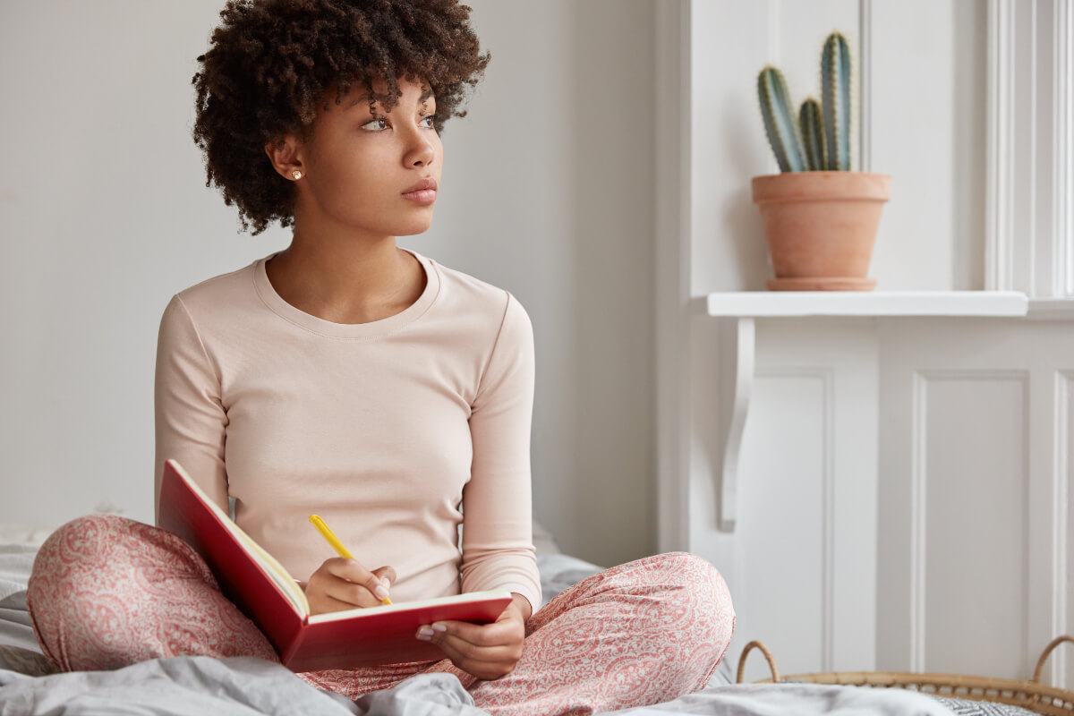 Woman sits in her bed writing in her journal - sticking to her routines even during the holidays