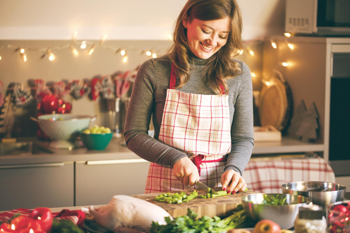 A woman happily preparing a holiday meal in the kitchen because nourishing food ca help your mental wellness during the holidays. 