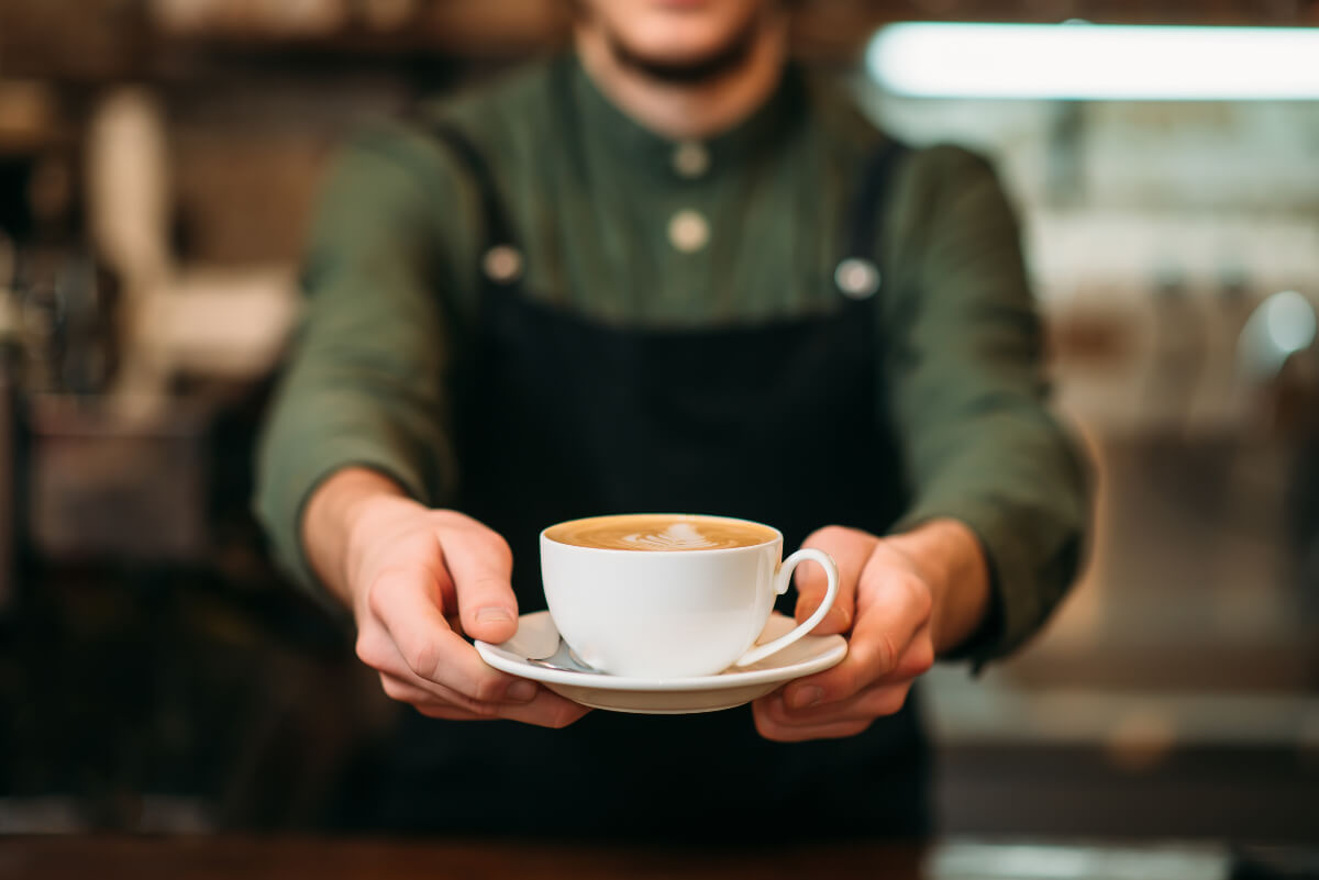 Pay it forward by paying for the coffee of the person behind you. Pictured: Hands holding out a cappuccino. 