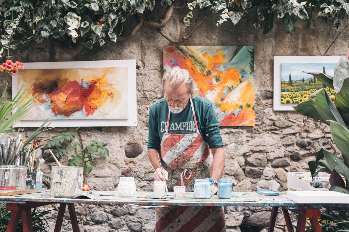 Beautiful, inspiring art is something to be grateful for. In this photo, a man paints on canvases outdoors. 