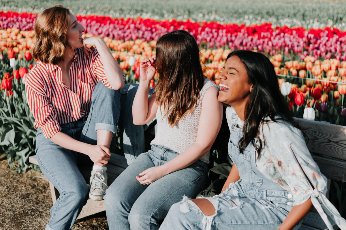 Three happy friends sit on a bench next to a field of tulips. Friends and family are something to be grateful for. 