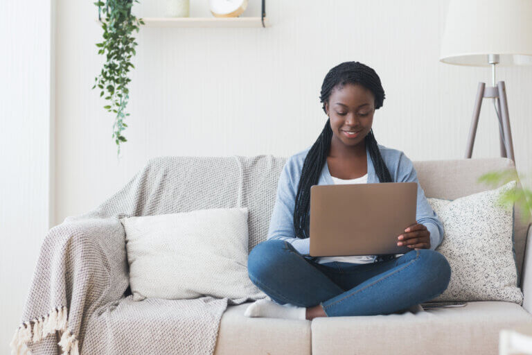 A woman sitting on a cozy sofa using her laptop.