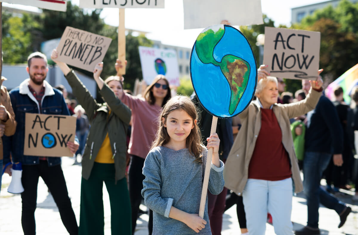 Climate change demonstrators hold up signs. A little girl holds up a sign of the Earth.