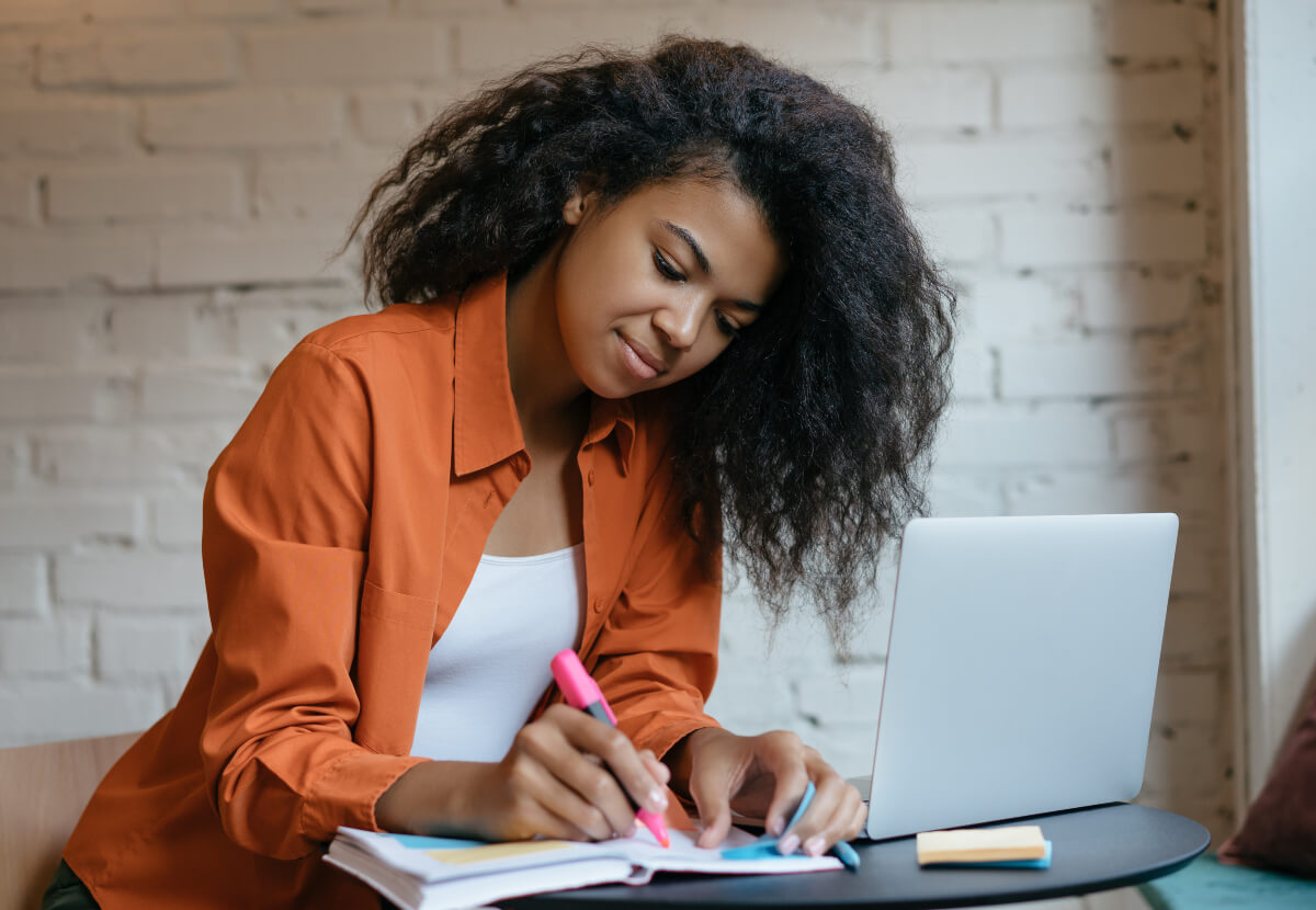 Woman sitting at a desk highlighting notes in a planner.