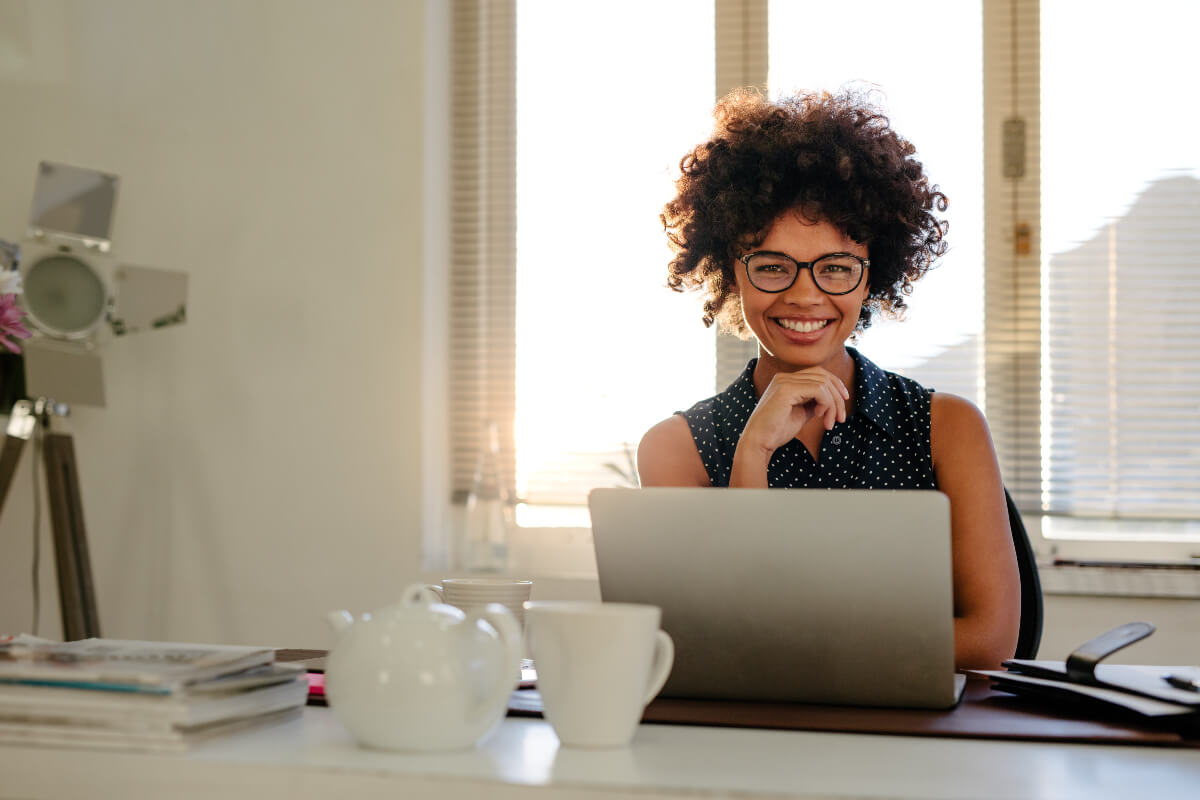 Person sitting at their desk smiling with a laptop and a cup of tea. They must be happy because of how great their work apps are. 