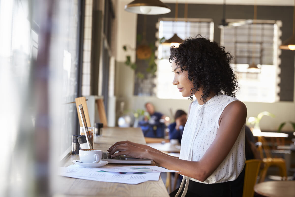 A woman reading a book at a coffee shop. Changing your environment is a New Year's Resolution tip to help you reach your goals. 