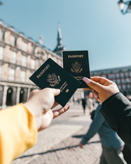 Two people holding their passports up with a scenic location in the background. A top travel tip is to bring along paper copies of your passport. 
