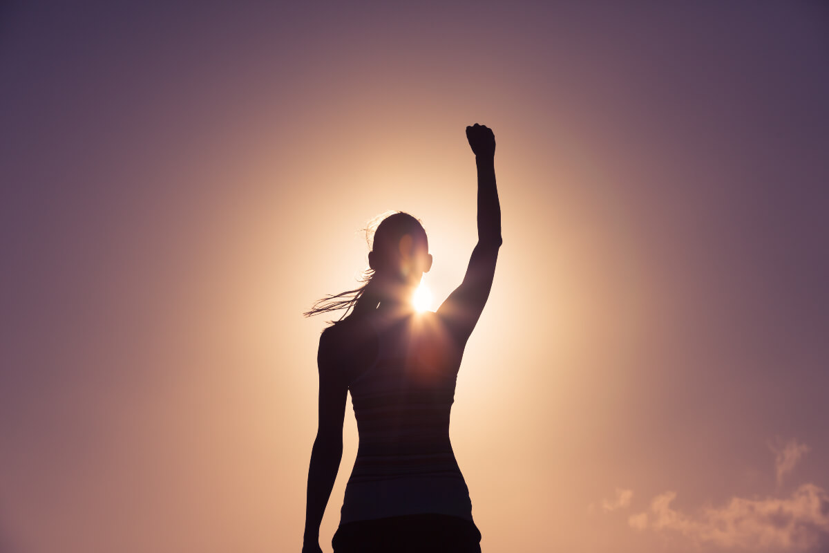 Silhouette of a person standing facing the sun with a fist raised. Now they look like their confidence has been boosted!