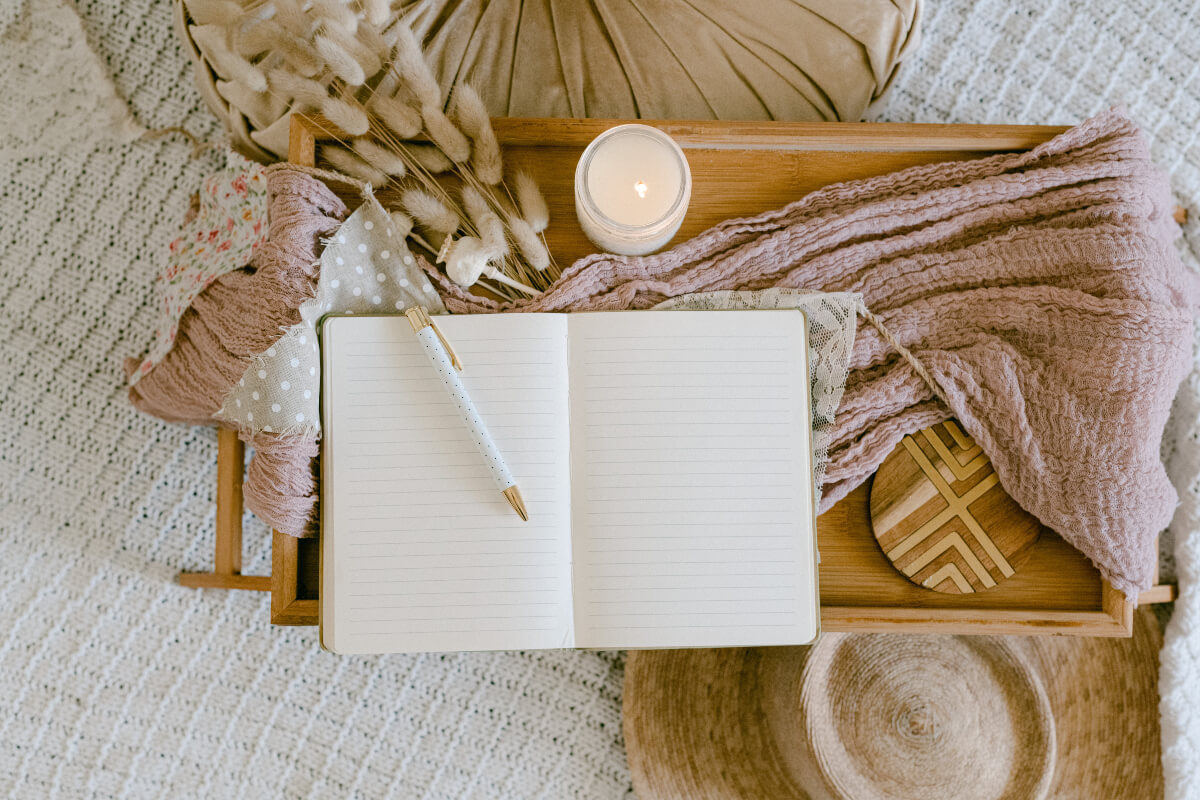 An open, blank journal and a white candle on a wooden tray