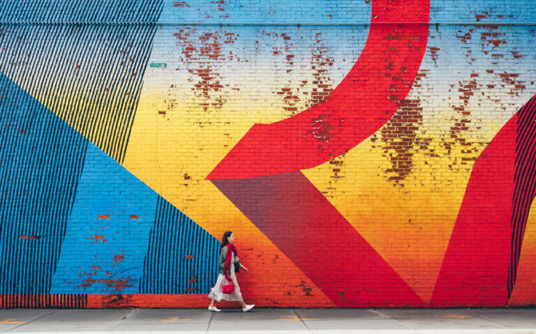 Woman walks past wall covered in red, blue, and yellow graffiti art