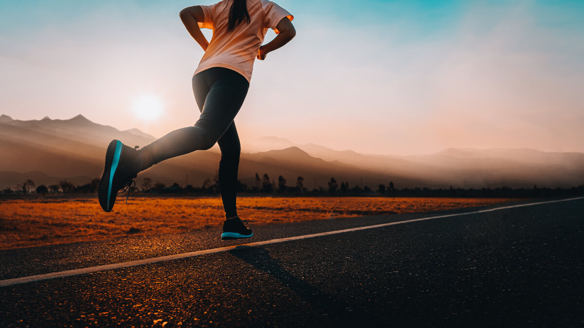 Person jogging down a road with mountains and the sun rising in the background 