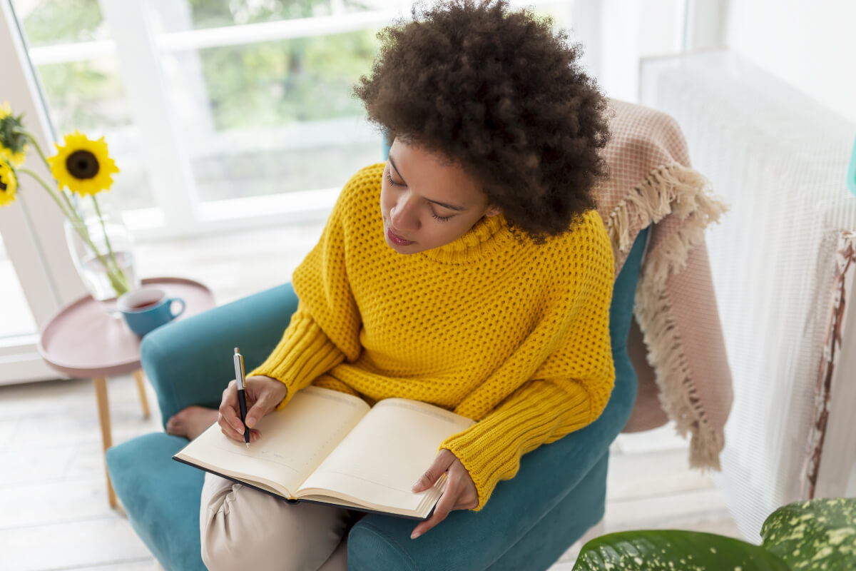Person in yellow sweater writes in a journal