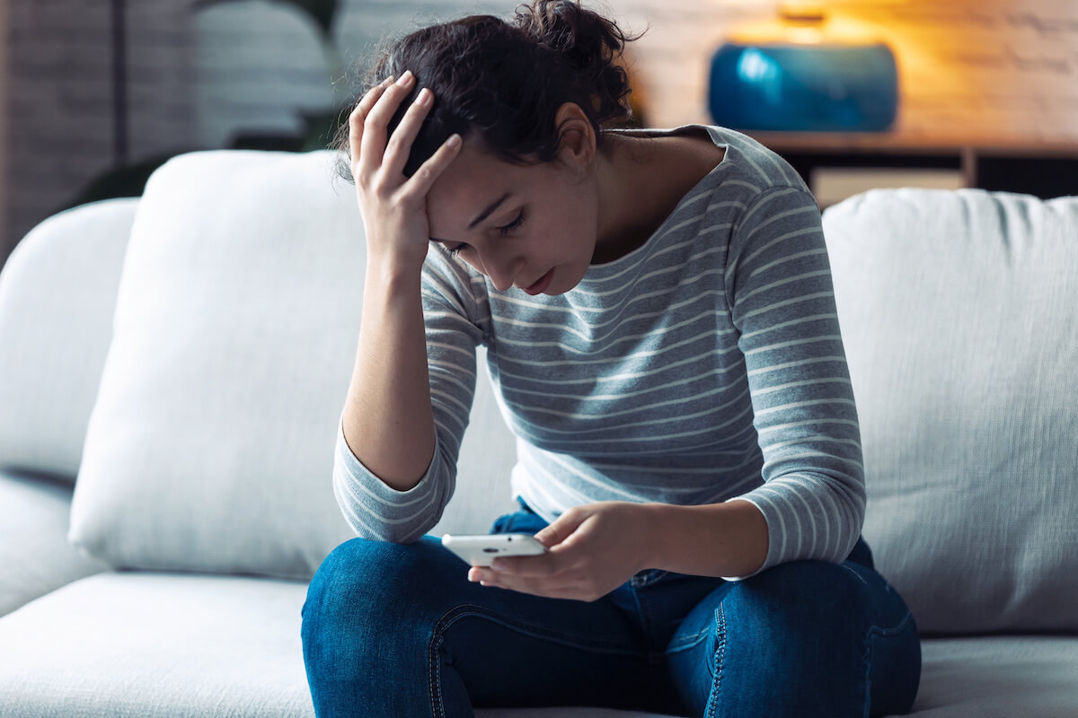 Shot of worried young woman using her mobile phone while sitting on sofa in the living room at home.