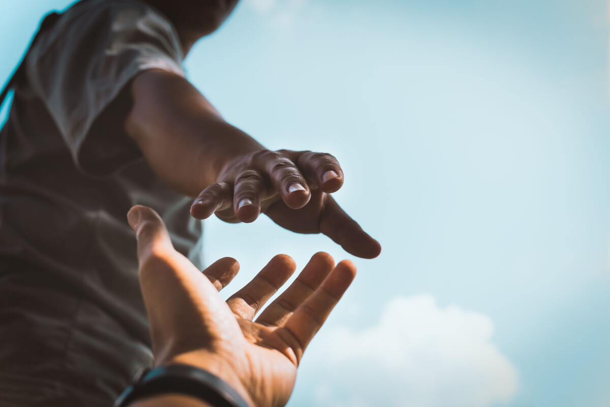 Two outstretched hands reaching out to one another with a blue, cloudy sky in the background. Another meaningful way to honour Black History Month in 2022 is to give to a charity that supports Black communities. 