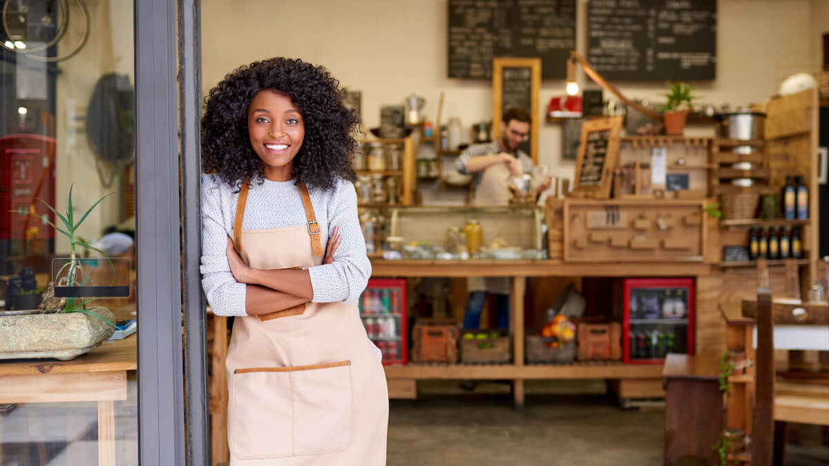 A female African Canadian business owner standing in front her store.