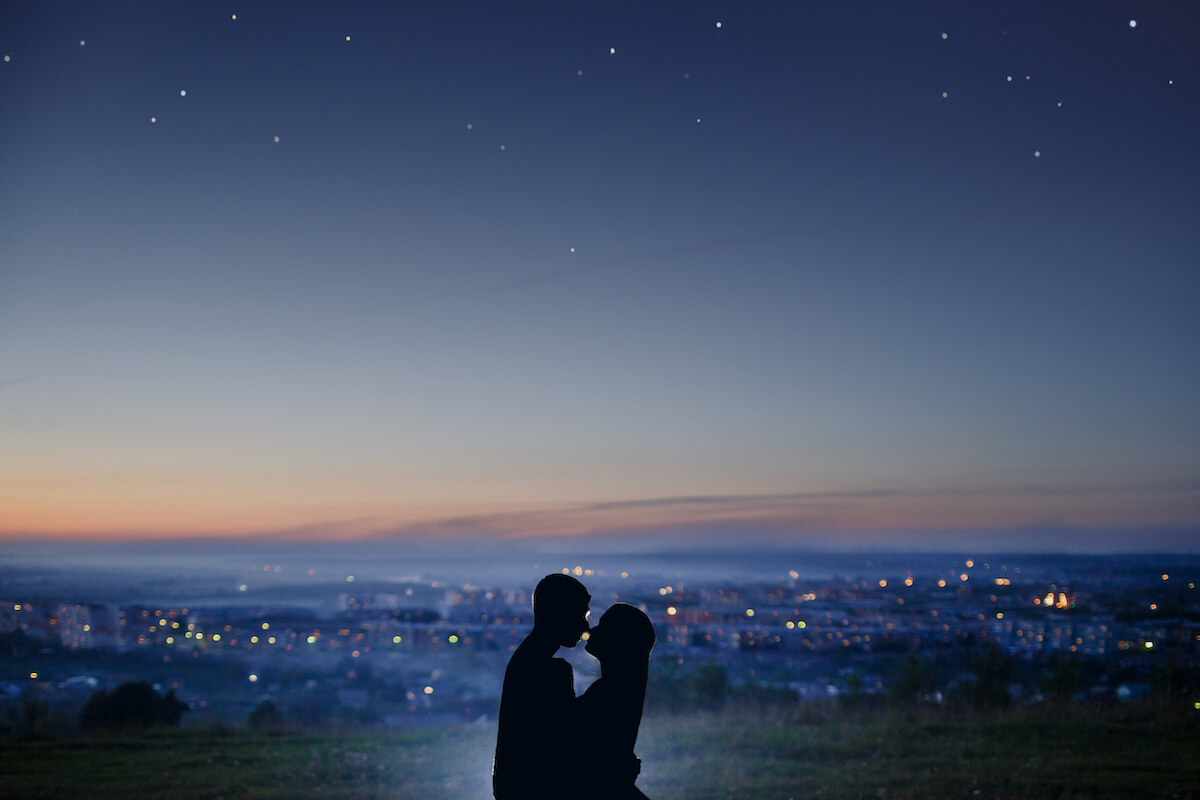 Silhouette of a couple in love against the background of a night city, stars and horizon. Concept is a date on the roof, the first love