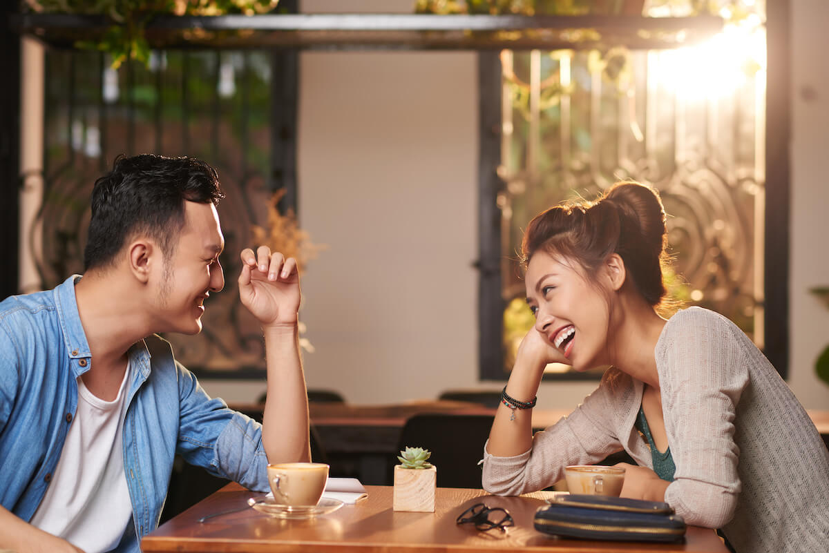 Side view portrait of laughing Asian couple enjoying date in cafe