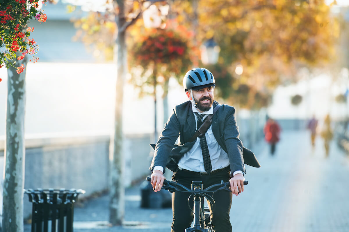 Hipster businessman commuter with electric bicycle traveling home from work in city at sunset. 