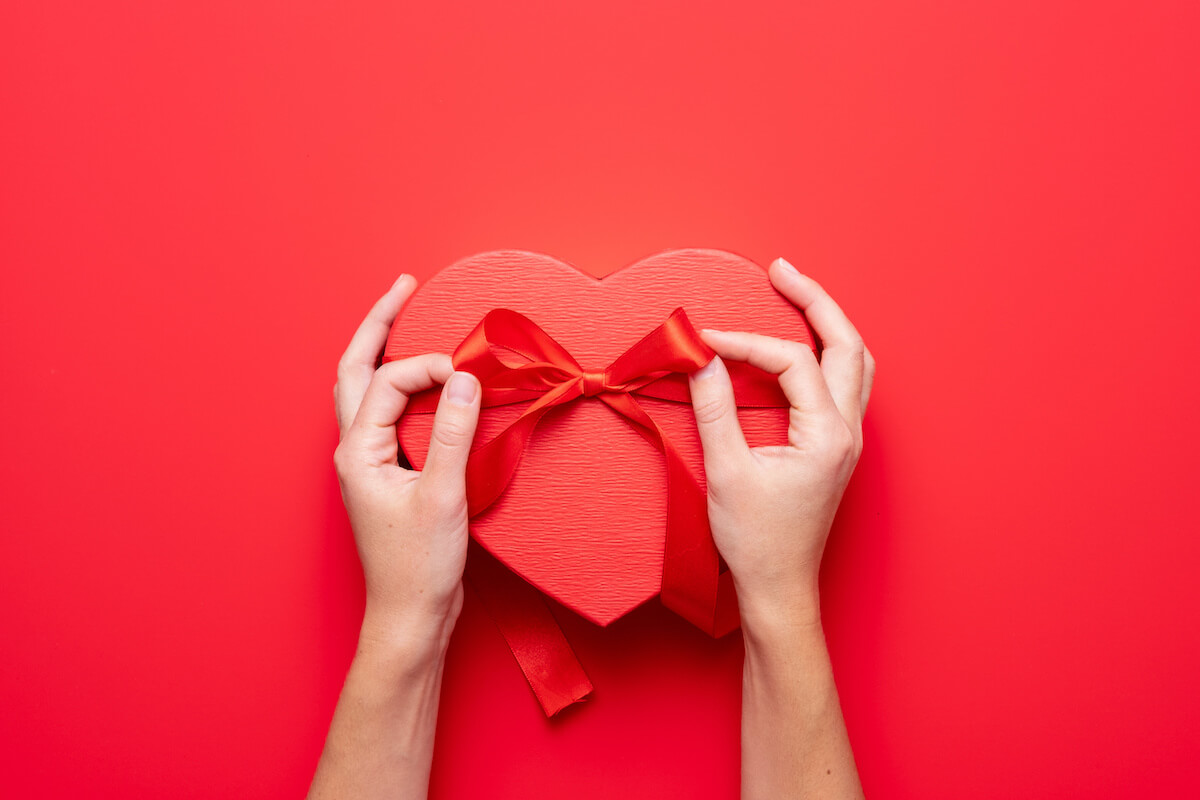 Top view of female hands holding a gift heart shape. Presents for valentine day, birthday, mother's day. Flat lay. Symbol of love. Valentines day background with a gift boxes on concrete board.