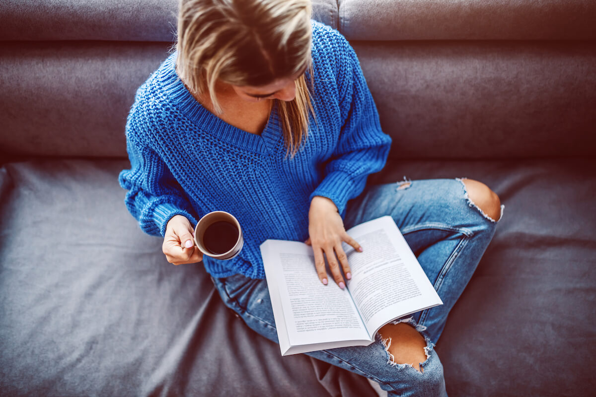 Lady reading a book and drinking coffee on a couch 