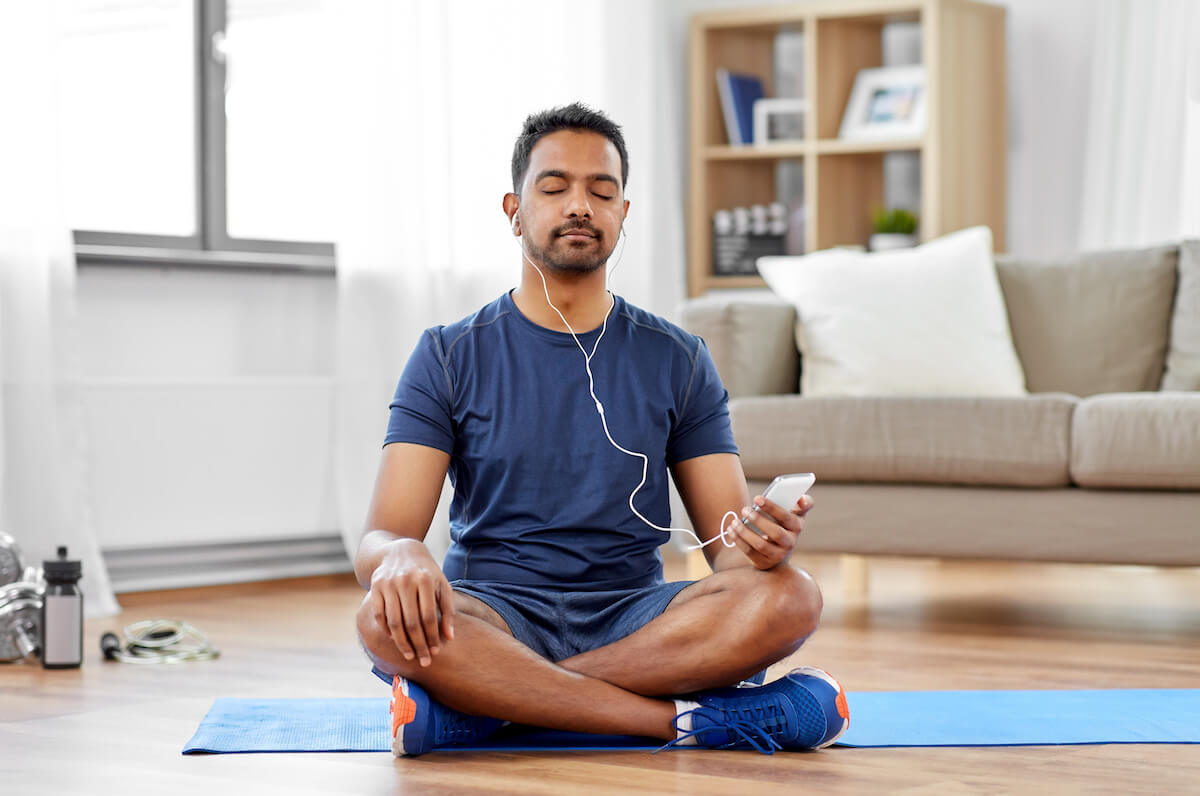 sport, technology and healthy lifestyle concept - indian man in earphones listening to music on smartphone at home