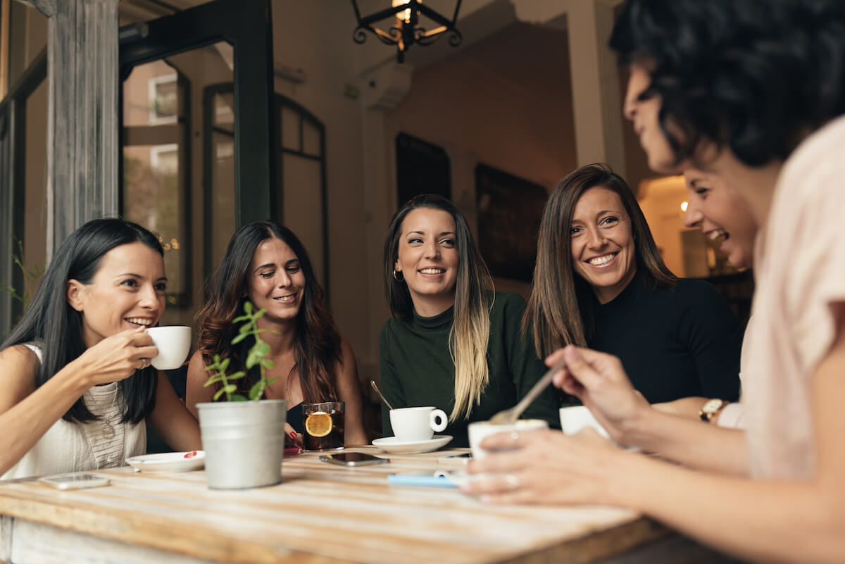 Six beautiful women drinking coffee and chatting in cafe