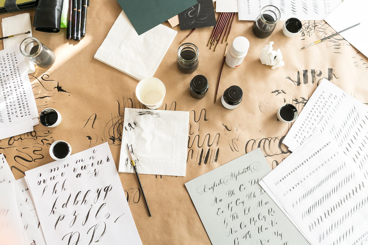 Calligraphy sheets, nibs, paper, ink and pens on a kraft background. Lettering calligraphy workshop. lLetters of the English alphabet written with a paint brush. Concept hobby. top view, flat lay.