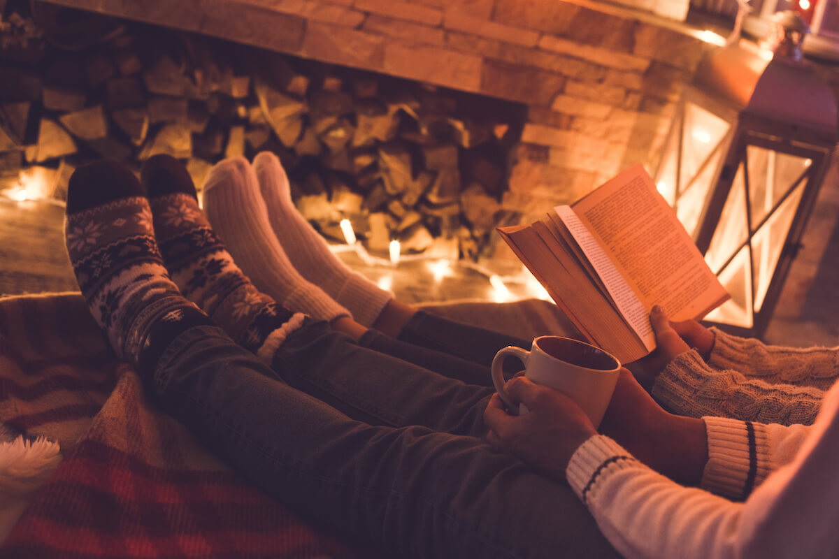Young man and woman near the fireplace at home together sitting drinking hot cocoa and reading book