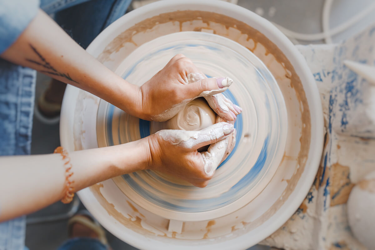 Top view of hands with clay making of a ceramic pot on the pottery wheel, hobby and leisure with pleasure concept