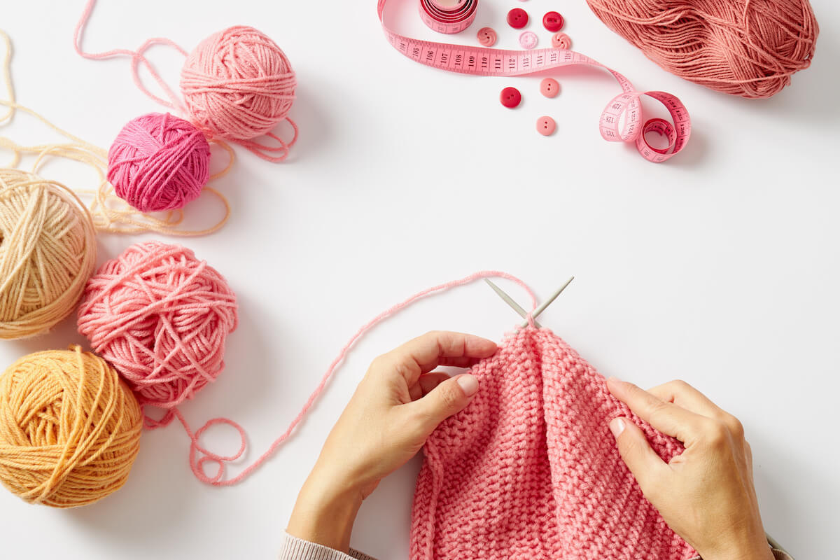 Female hands knitting with pink wool, on a white background, top view