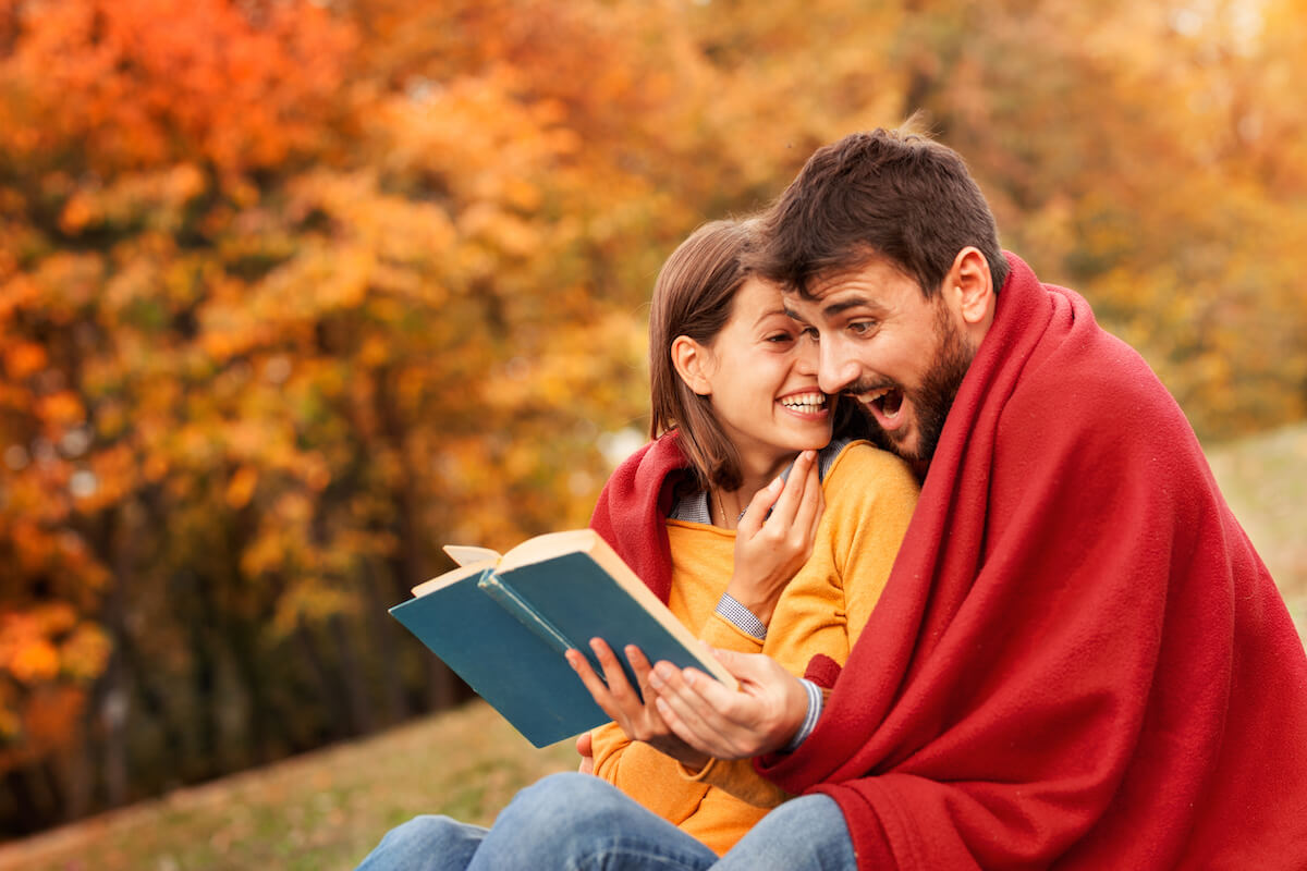 Loving couple wrapped with a blanket reading very diverting book