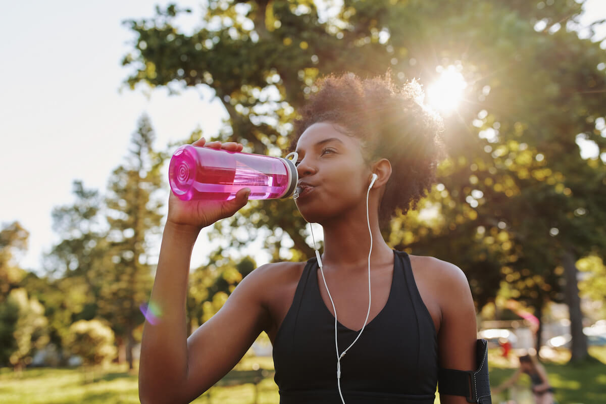 Woman athlete takes a break, drinking water from a reusable water bottle on a hot summers day