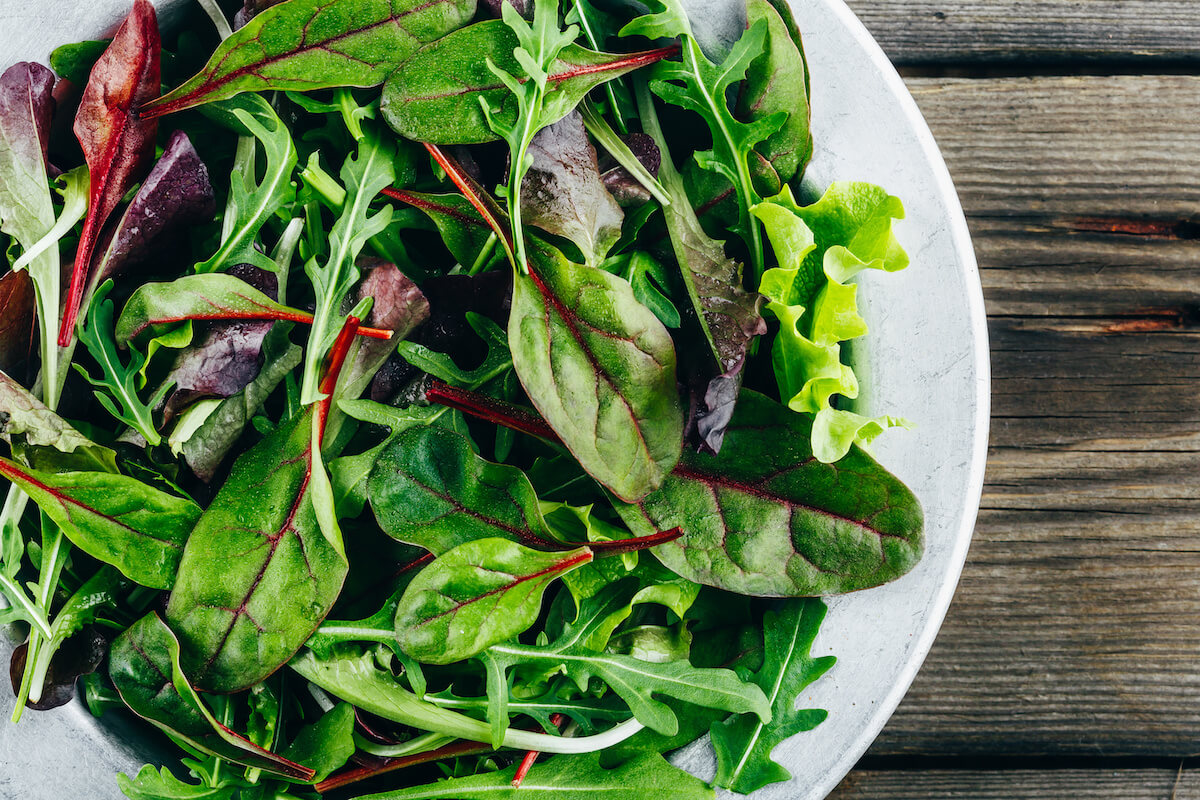 Mix of fresh green salad leaves with arugula, lettuce, spinach and beets on wooden rustic background. Top view