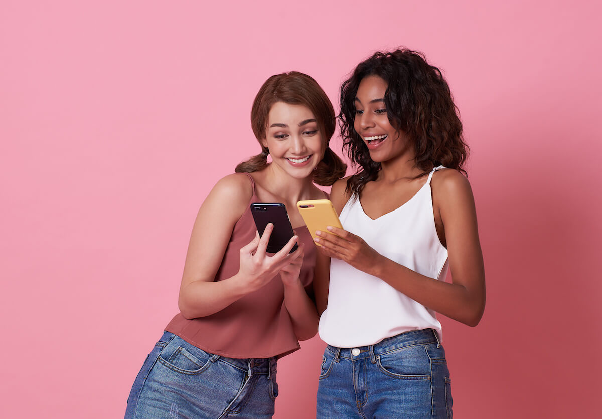 Two happy women friends playing and sharing social media in a smart phone.