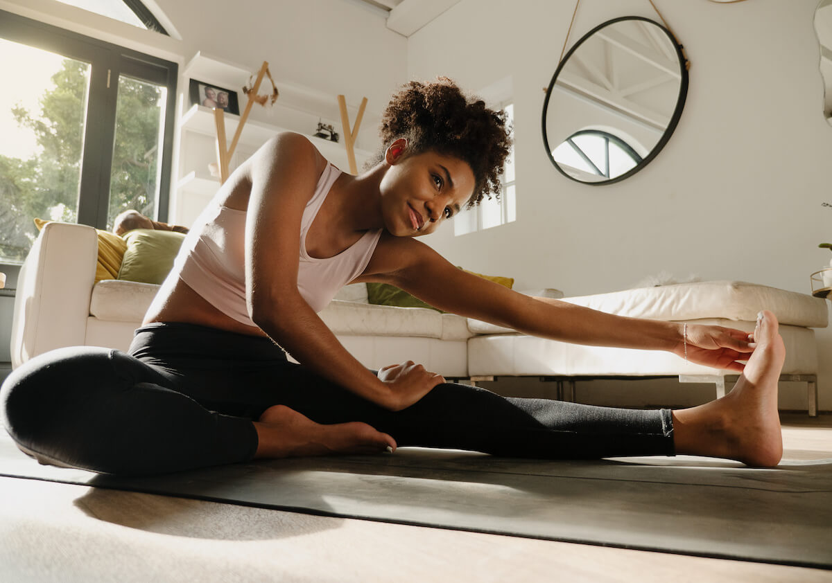 Beautiful mixed race female working out in the lounge at home, stretching legs and warming up